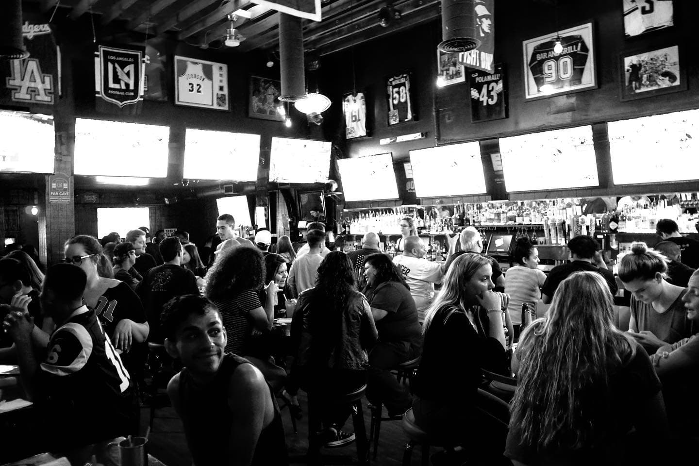 The bar packed wall to wall under a row of screens, shot in black and white