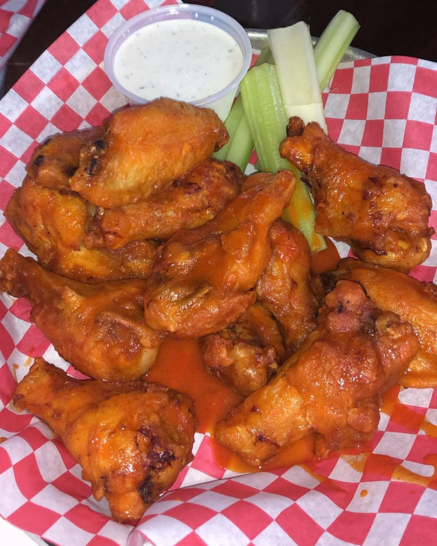 A basket of Rocco's wings in red checkered paper, served with celery and ranch