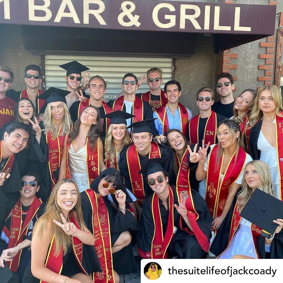 A large group of graduates in caps, gowns and cardinal sashes packed under the 901 Bar & Grill sign