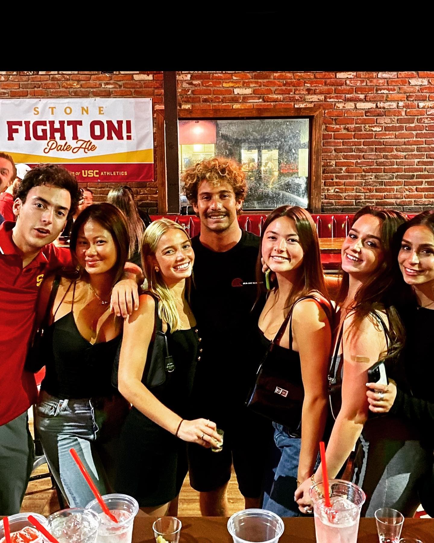 A group under the Fight On sign against the brick wall inside the bar